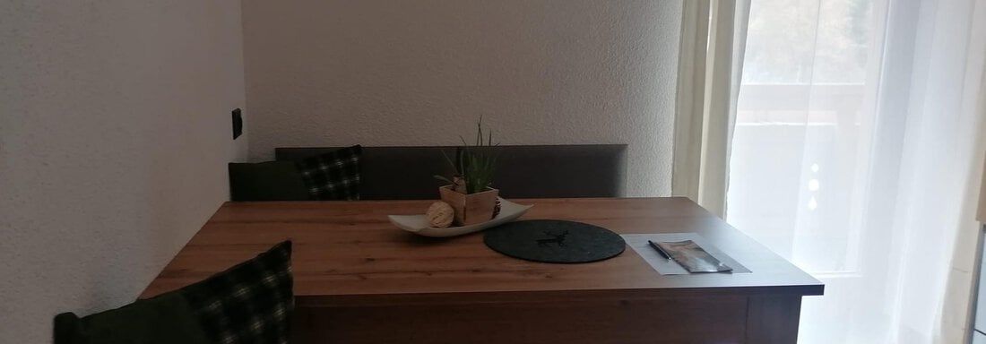 A cozy dining area with a wooden table and a bench. Bright curtains let light in and create an inviting atmosphere. - Gästehaus Sternberger - Sölden