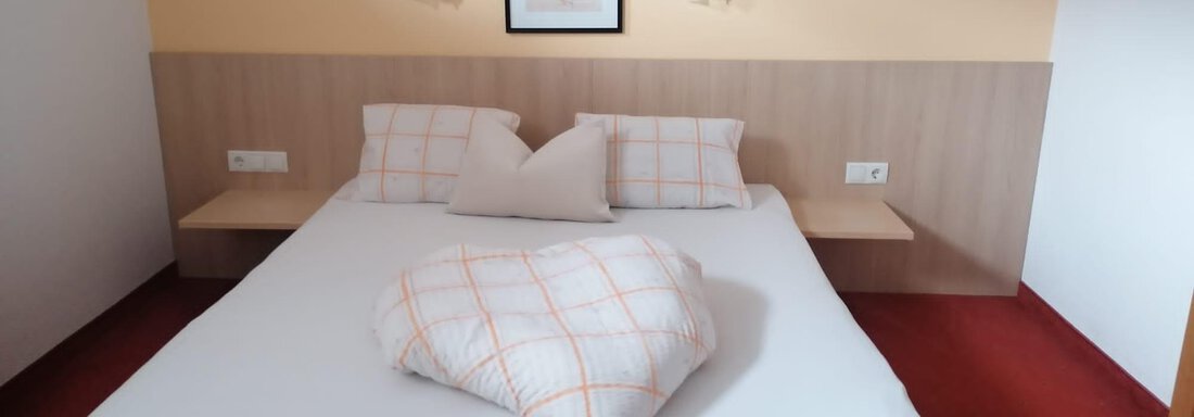 A cozy bedroom with a large double bed and additional pillows. The walls are painted in soft color tones, and there is a decorative picture. - Gästehaus Sternberger - Sölden