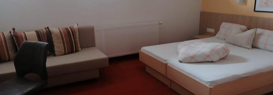 A cozy room with a double bed and a seating area. The walls are painted in soft colors, and it is bright and inviting. - Gästehaus Sternberger - Sölden