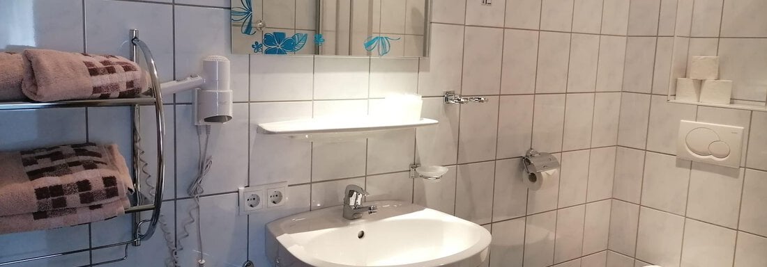 A modern bathroom with white tiles and a hand basin. On the left side, towels and a mirror are visible. - Gästehaus Sternberger - Sölden