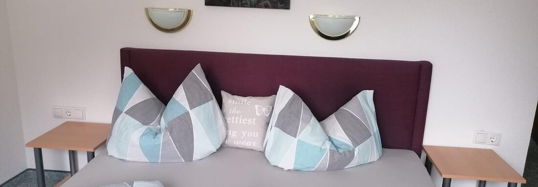 A cozy bedroom with a large bed and colorful pillows. A picture with floral motifs hangs on the wall. - Gästehaus Sternberger - Sölden