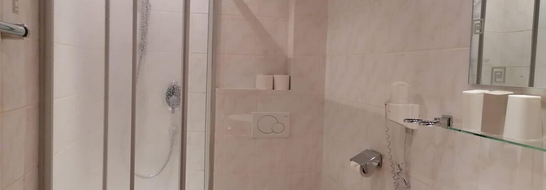 A modern bathroom with a shower niche and a toilet. The walls are tiled in light colors, and the fixtures are simple and functional. - Gästehaus Sternberger - Sölden