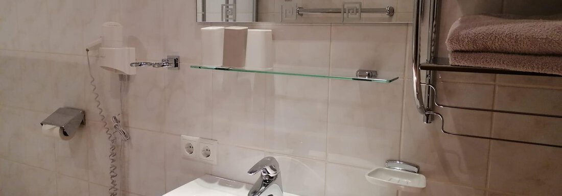 A modern bathroom with a white sink unit and a mirror. Towels are neatly stored on a shelf. - Gästehaus Sternberger - Sölden