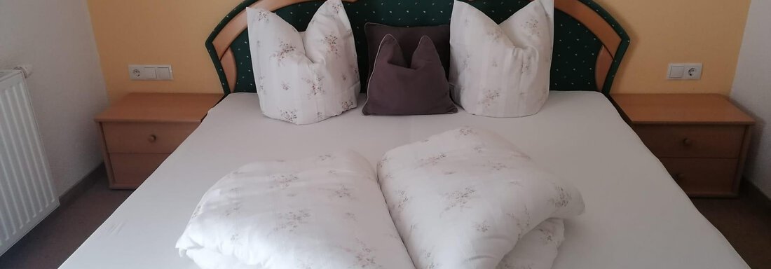 A cozy bedroom with a large bed and decorative pillows. The pillows are folded into hearts and create a romantic atmosphere. - Gästehaus Sternberger - Sölden