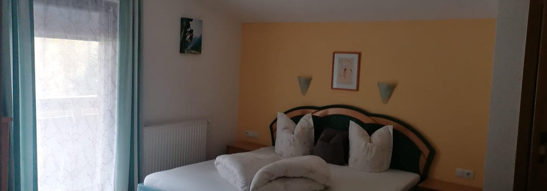 A cozy bedroom with a large bed and decorative pillows. The walls are painted in soft colors and the window lets in plenty of daylight. - Gästehaus Sternberger - Sölden
