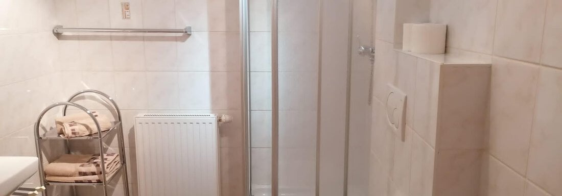 A modern bathroom with white tiles and a clear shower. It also includes towels and a heating system. - Gästehaus Sternberger - Sölden