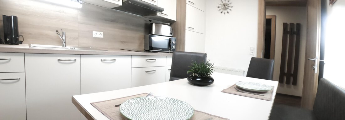A modern kitchen with a dining table and chairs. The walls are light and the lighting creates a friendly atmosphere. - Gästeheim Schmiedhof - Sölden