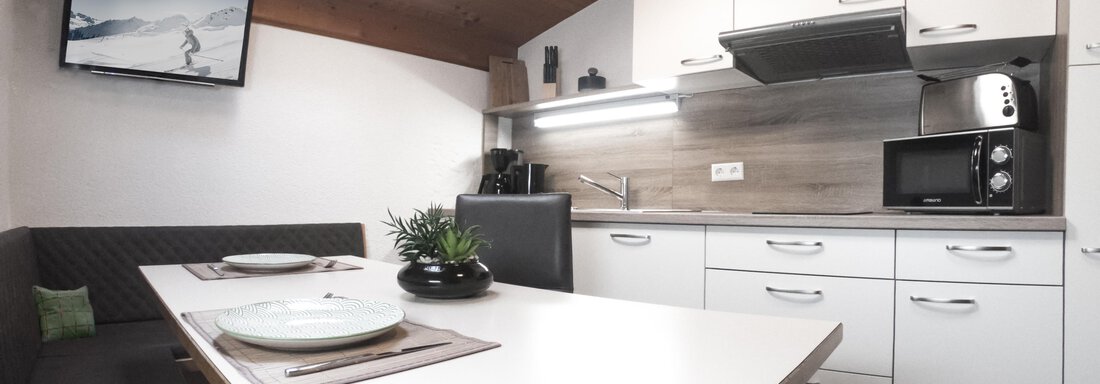 A modern kitchen with a bright dining area. It includes appliances such as a microwave and a television on the wall. - Gästeheim Schmiedhof - Sölden