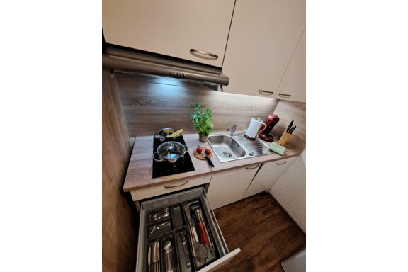 A modern kitchen with a stove, a sink, and fresh herbs. In the drawer, cooking utensils are neatly organized. - Gästeheim Schmiedhof - Sölden