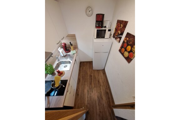 A small, modern kitchen with white cabinets and wooden flooring. On the countertop, there is a coffee machine, a microwave, and various kitchen utensils. - Gästeheim Schmiedhof - Sölden