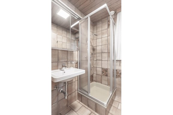 A modern bathroom with a shower cabin and a sink. The walls are covered with bright tiles. - Gästeheim Schmiedhof - Sölden