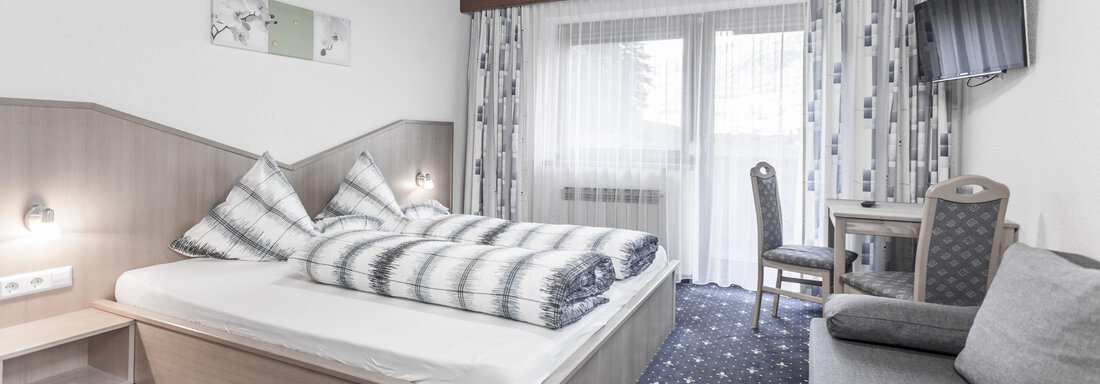 A cozy room with a double bed and modern furniture. Large windows let in plenty of light and offer a beautiful view outside. - Gästeheim Schmiedhof - Sölden