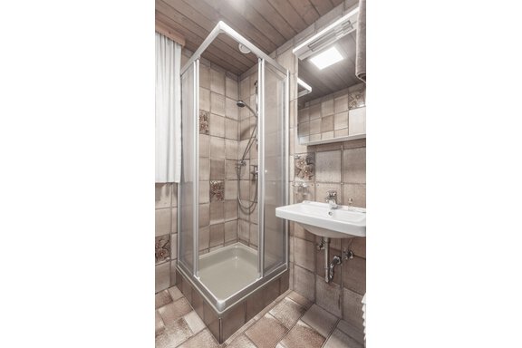 A modern bathroom with a glass shower and a sink. The walls are designed with light tiles. - Gästeheim Schmiedhof - Sölden