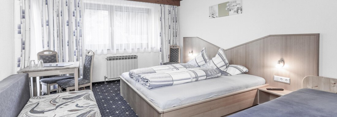 A cozy hotel room with two beds and a small table. The window provides plenty of daylight and the decor is simple and inviting. - Gästeheim Schmiedhof - Sölden