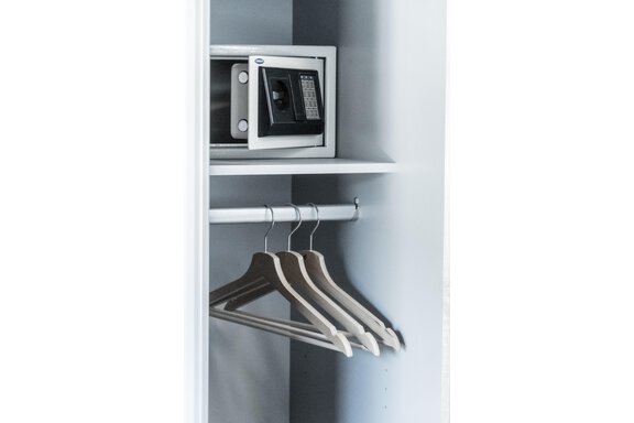 An open wardrobe with a safe and three hangers. The wardrobe has a bright, modern aesthetic. - Gästeheim Schmiedhof - Sölden