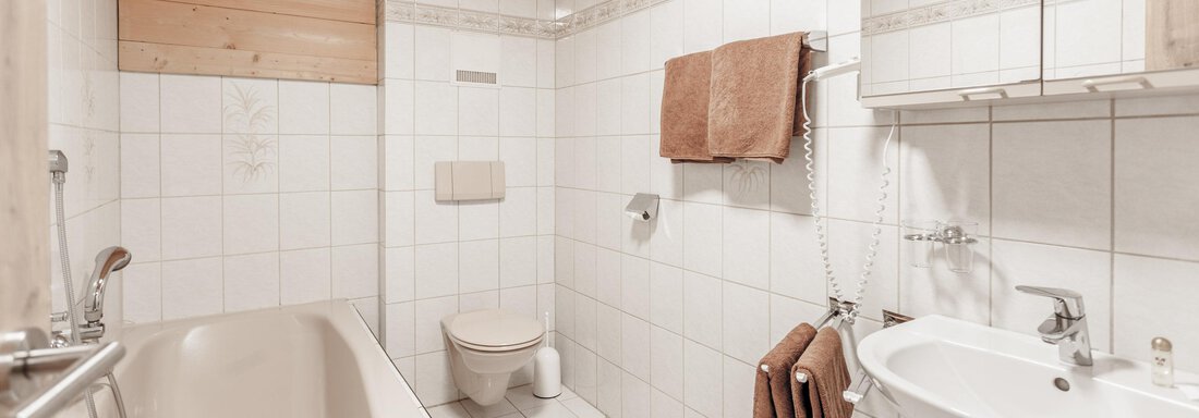 Schmiedhof_Sölden_Contrast_innen-7069 A modern bathroom with white tiles and a wooden ceiling. There is a bathtub, a sink, and towels. - Gästeheim Schmiedhof - Sölden