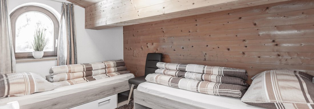 A cozy room with two beds and wood paneling. Large windows provide plenty of daylight. - Gästeheim Schmiedhof - Sölden