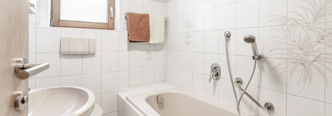 A simple bathroom with a bathtub and a sink. Bright tiles and a window provide light and airiness. - Gästeheim Schmiedhof - Sölden