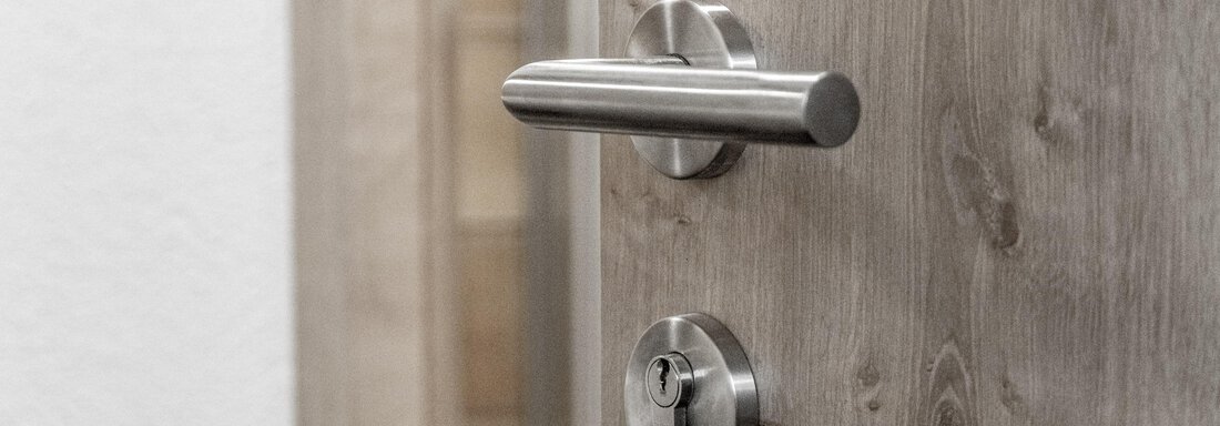 A modern door lock and a stainless steel door handle. The door has a wood look and is brightly designed. - Gästeheim Schmiedhof - Sölden