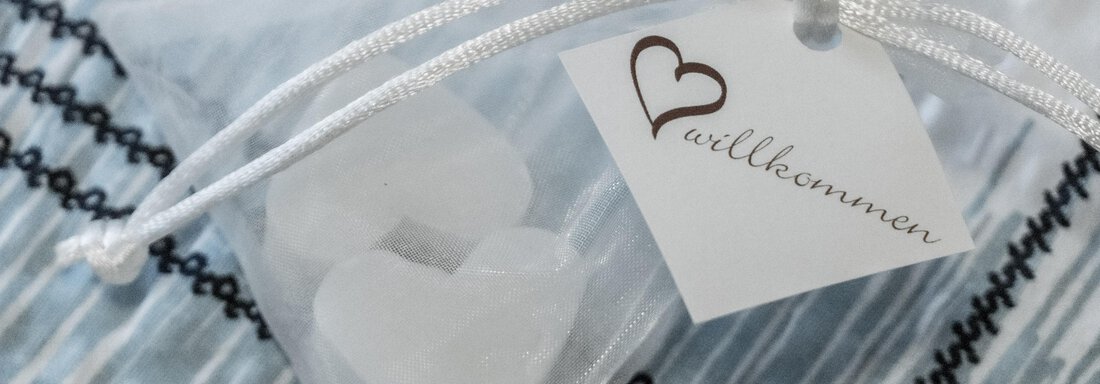 A transparent pouch with white sugar balls shaped like hearts and a tag. The tag reads "welcome." - Gästeheim Schmiedhof - Sölden
