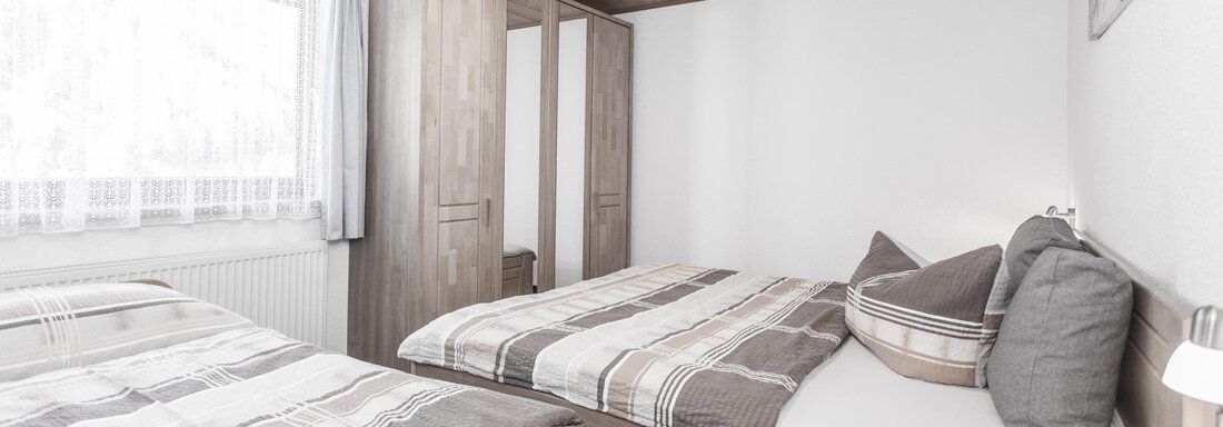 A cozy bedroom with two beds and a wooden ceiling. The rooms are bright and simply furnished, with plenty of storage space. - Gästeheim Schmiedhof - Sölden