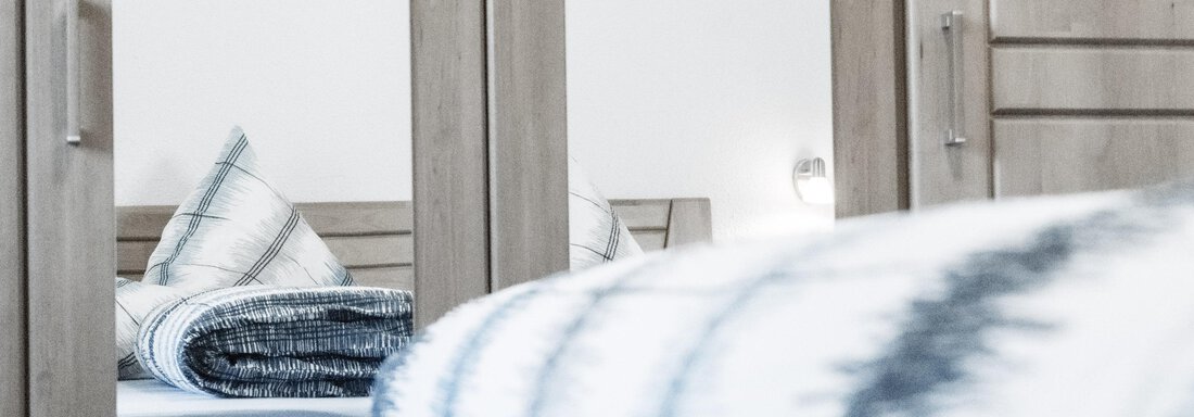 A cozy bedroom with a bed and a blanket. In the background, there is a mirror that reflects the furnishings. - Gästeheim Schmiedhof - Sölden