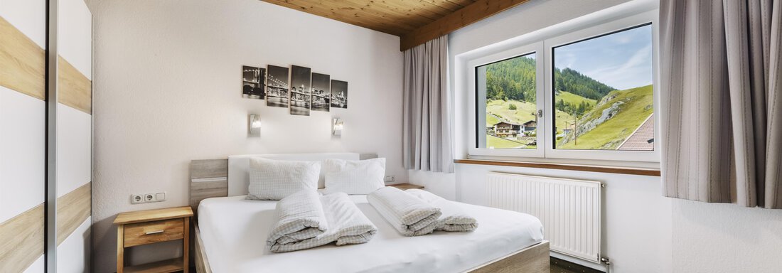 _F0A8073 A modern bedroom with a large bed and fresh towels. Through the window, a green landscape can be seen. - Gasthof Granstein - Sölden