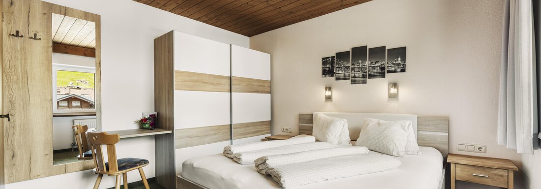 A modern bedroom with a large bed and wooden elements. There is a desk and a chair, as well as a built-in wardrobe. - Gasthof Granstein - Sölden