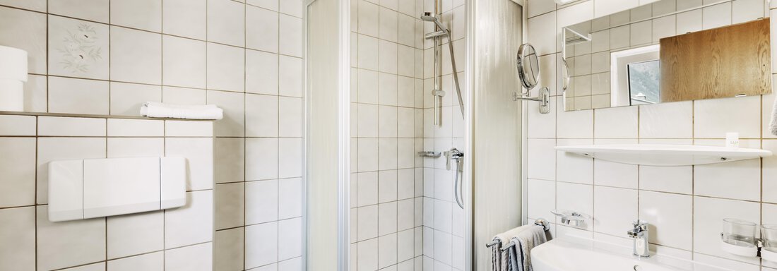 A modern bathroom with a shower cabin, a sink, and a large mirror. The walls are tiled and the ceiling is made of wood. - Gasthof Granstein - Sölden