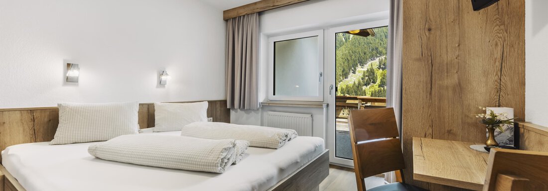 _F0A8229 A modern hotel room with a double bed and two blankets. The room has large windows that lead to a balcony with a view of the mountains. - Gasthof Granstein - Sölden