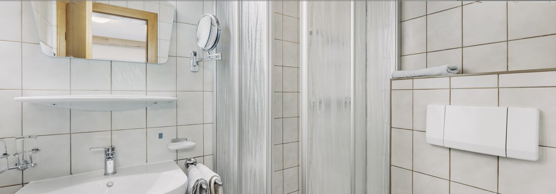 A modern bathroom with a shower, a sink, and a large mirror. The walls are lined with bright tiles, creating a friendly atmosphere. - Gasthof Granstein - Sölden