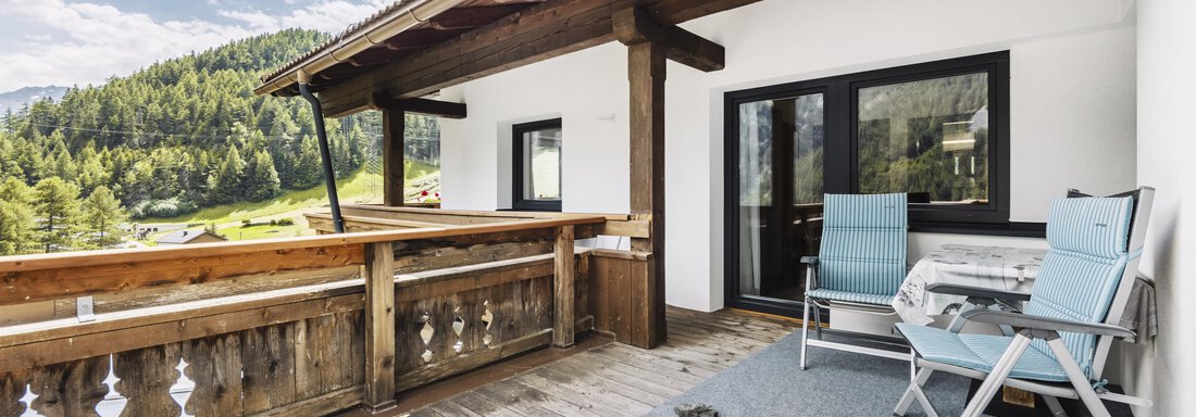 A cozy balcony with wooden cladding and two chairs. In the background, green hills and a clear sky can be seen. - Gasthof Granstein - Sölden