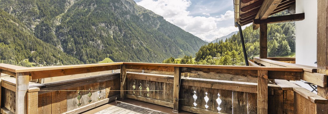 A wooden terrace overlooking majestic mountains and a green landscape. The sky is partly cloudy and conveys a calm atmosphere. - Gasthof Granstein - Sölden