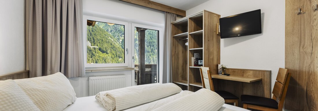 A modern room with two single beds, a desk, and a television. Through the window, a beautiful view of the mountains is visible. - Gasthof Granstein - Sölden