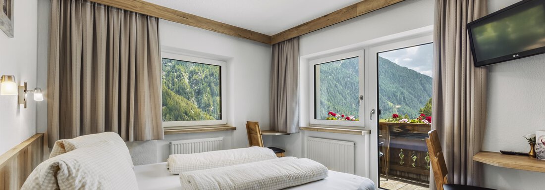 A bright bedroom with a double bed and a view of the mountains. There is a small balcony and a television on the wall. - Gasthof Granstein - Sölden