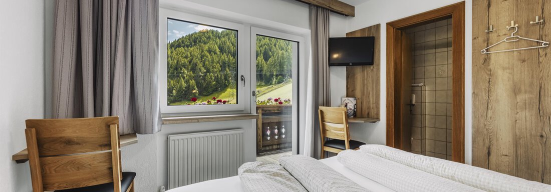 A cozy room with two beds and wooden decor. Large windows offer a view of the green surroundings. - Gasthof Granstein - Sölden