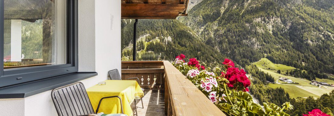 A balcony with a view of green mountains and blooming flowers. Two chairs and a table invite you to relax. - Gasthof Granstein - Sölden