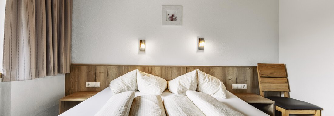 A cozy bedroom with two single beds and soft lighting. The walls are bright, and the wood décor gives the room a warm atmosphere. - Gasthof Granstein - Sölden