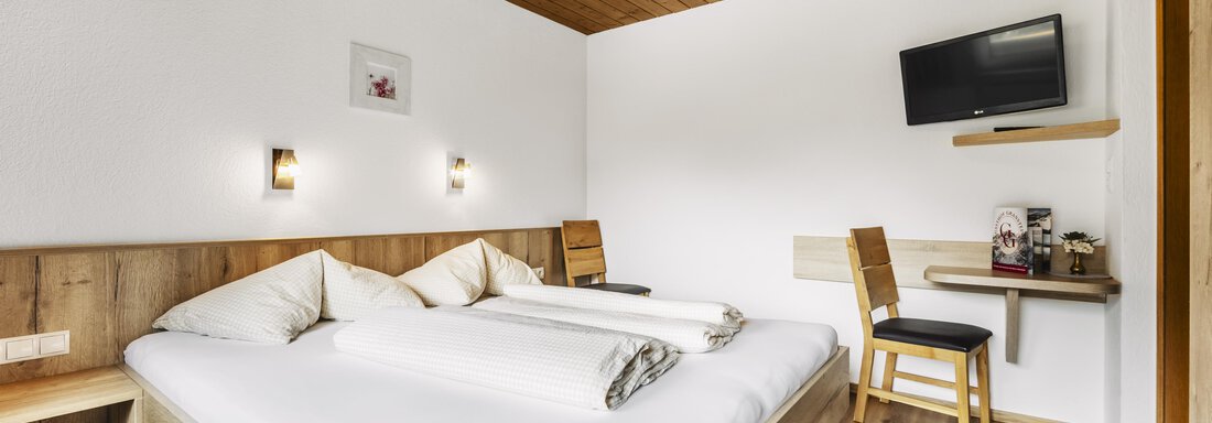 A cozy bedroom with a double bed and wooden paneling.  
The room includes a table, chairs, and a television on the wall. - Gasthof Granstein - Sölden