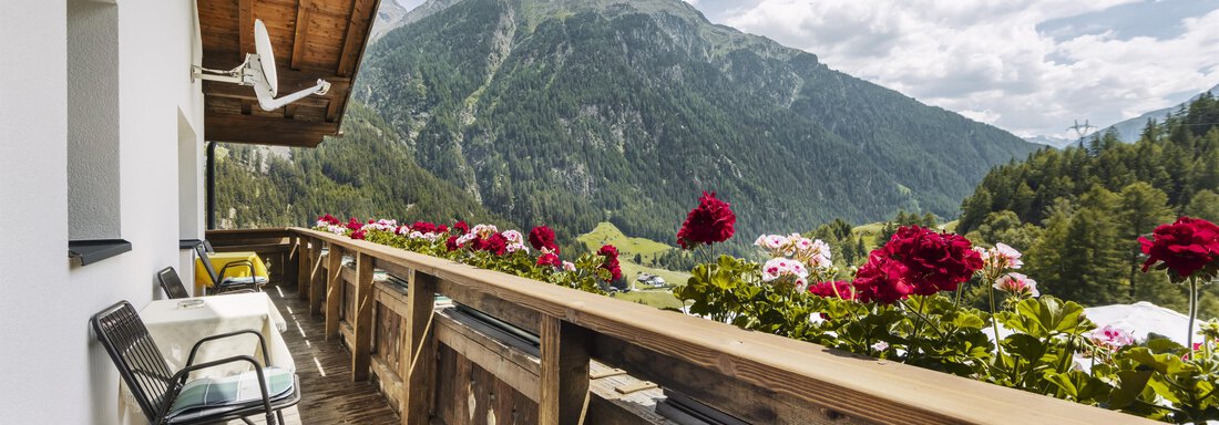 A balcony with colorful flowers and two chairs. In the background, mountains and a blue sky can be seen. - Gasthof Granstein - Sölden