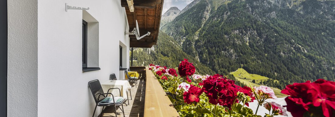 A balcony with flowers and a view of the mountains. The surroundings are green and wooded, under a clear sky. - Gasthof Granstein - Sölden