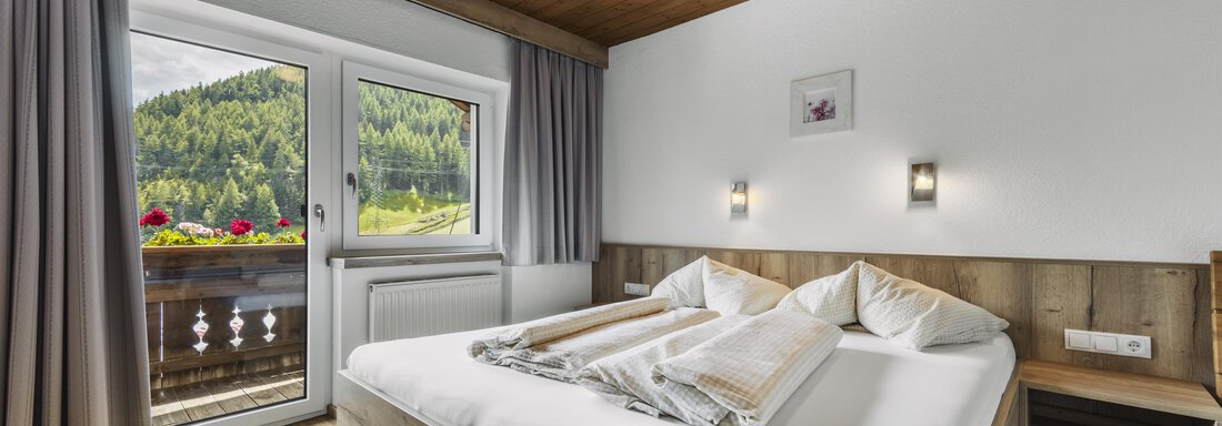 A bright and cozy bedroom with a wooden ceiling and modern furnishings. The balcony offers a lovely view of the surrounding nature. - Gasthof Granstein - Sölden