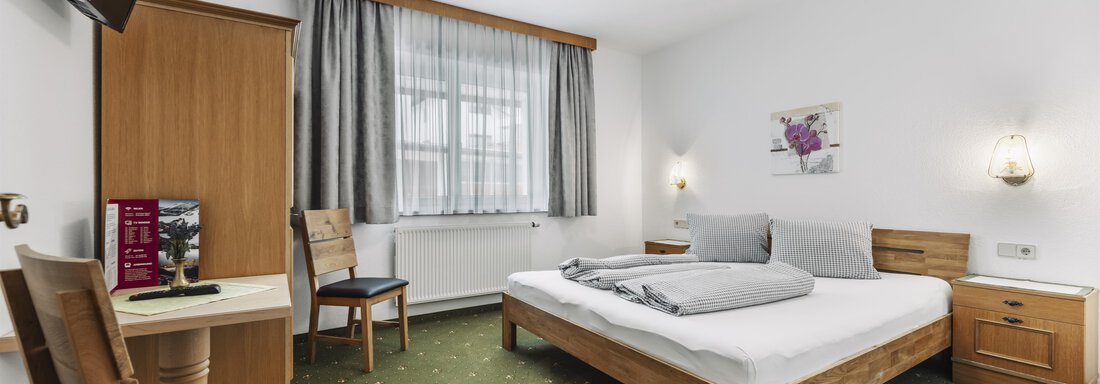 A simple and cozy room with a double bed and a television. There is a desk and chairs as well as a bright window front. - Gasthof Granstein - Sölden
