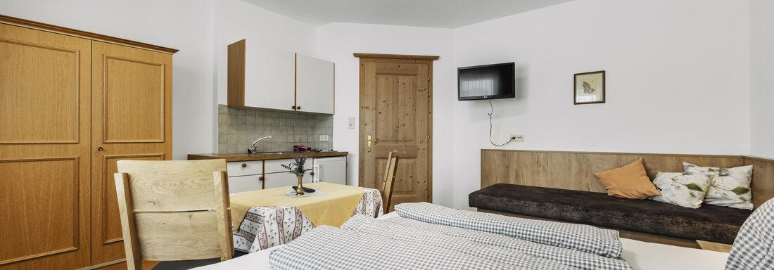 A cozy room with two beds, a small kitchen, and a television. The decor is functional and bright, with wooden details and an inviting atmosphere. - Gasthof Granstein - Sölden