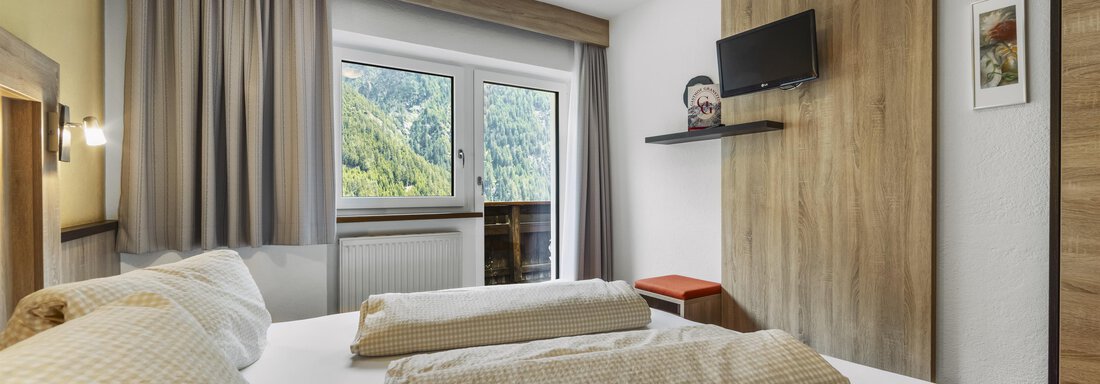 A cozy hotel room with a double bed and two large pillows. Through the window, you can see a green landscape. - Gasthof Granstein - Sölden
