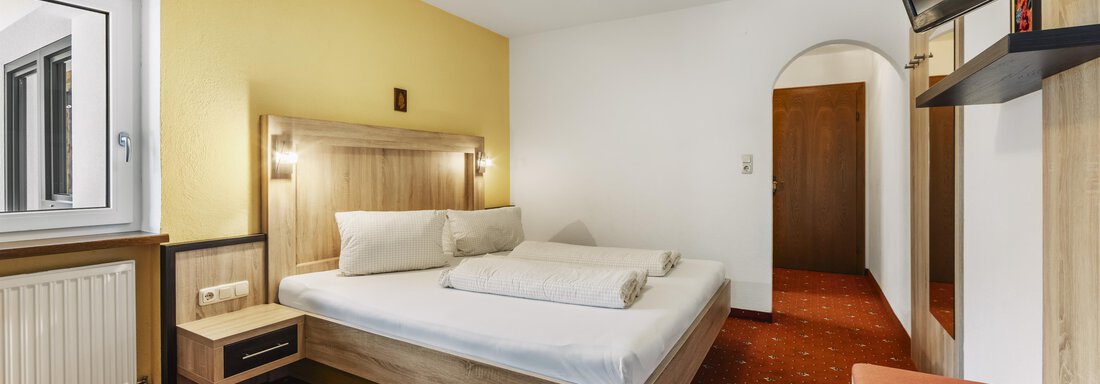 A bright hotel room with a double bed and a television. The walls are in soft colors, and there is a comfortable seating area. - Gasthof Granstein - Sölden