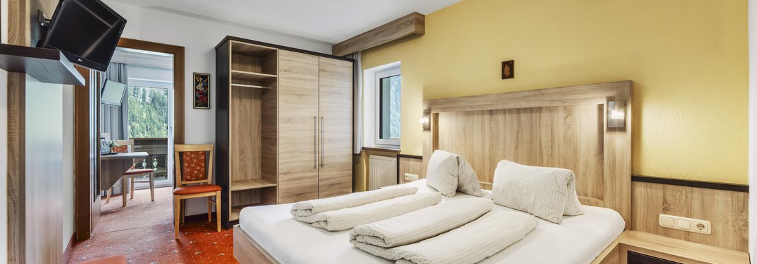 A cozy hotel room with a double bed, clean bed linen, and modern furniture. A television hangs on the wall, and there is access to a balcony. - Gasthof Granstein - Sölden