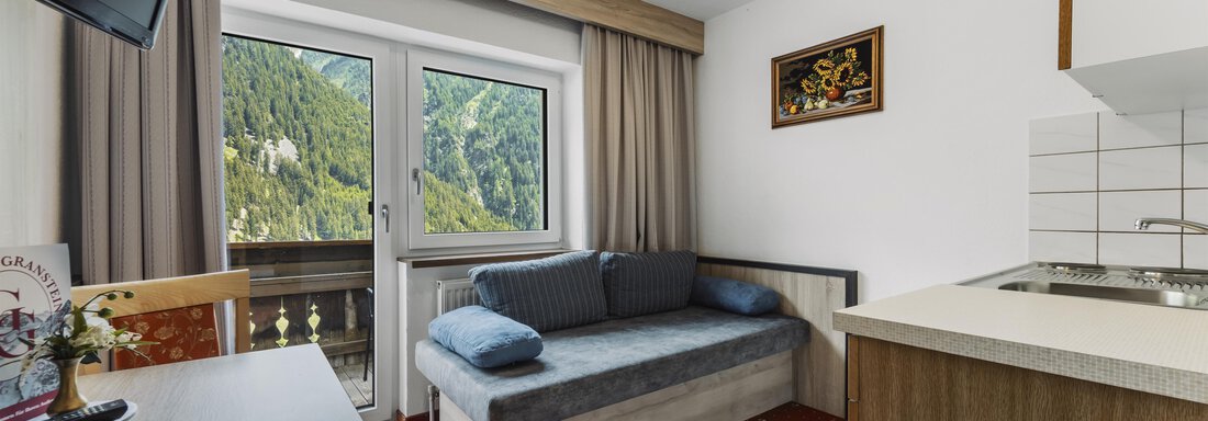 A cozy room with a sofa and a small kitchenette. Through the window, there is a beautiful view of the mountains. - Gasthof Granstein - Sölden