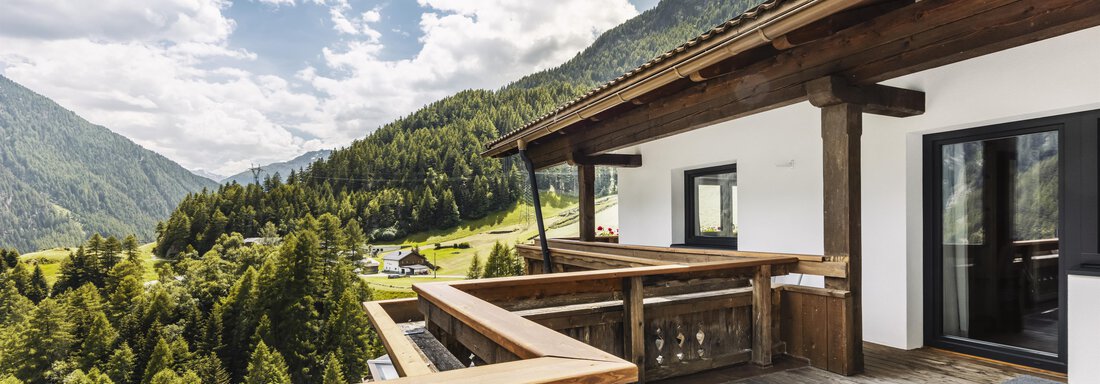A modern terrace with wooden railing and a view of green mountains. The sky is partially cloudy and invites relaxation. - Gasthof Granstein - Sölden