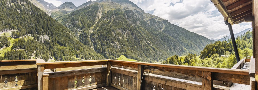 A wooden terrace overlooking majestic mountains and green forests. The sky is cloudy and a calm atmosphere prevails. - Gasthof Granstein - Sölden